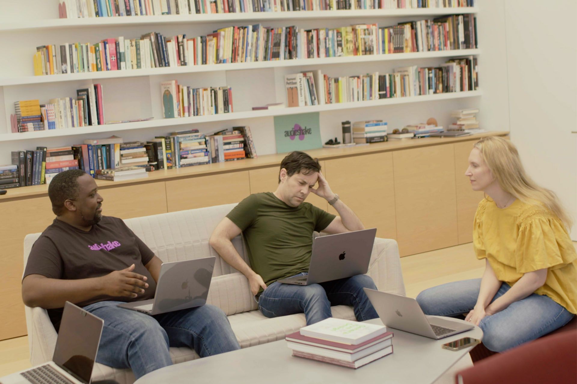 Three people talking on a couch in front of a bookshelf